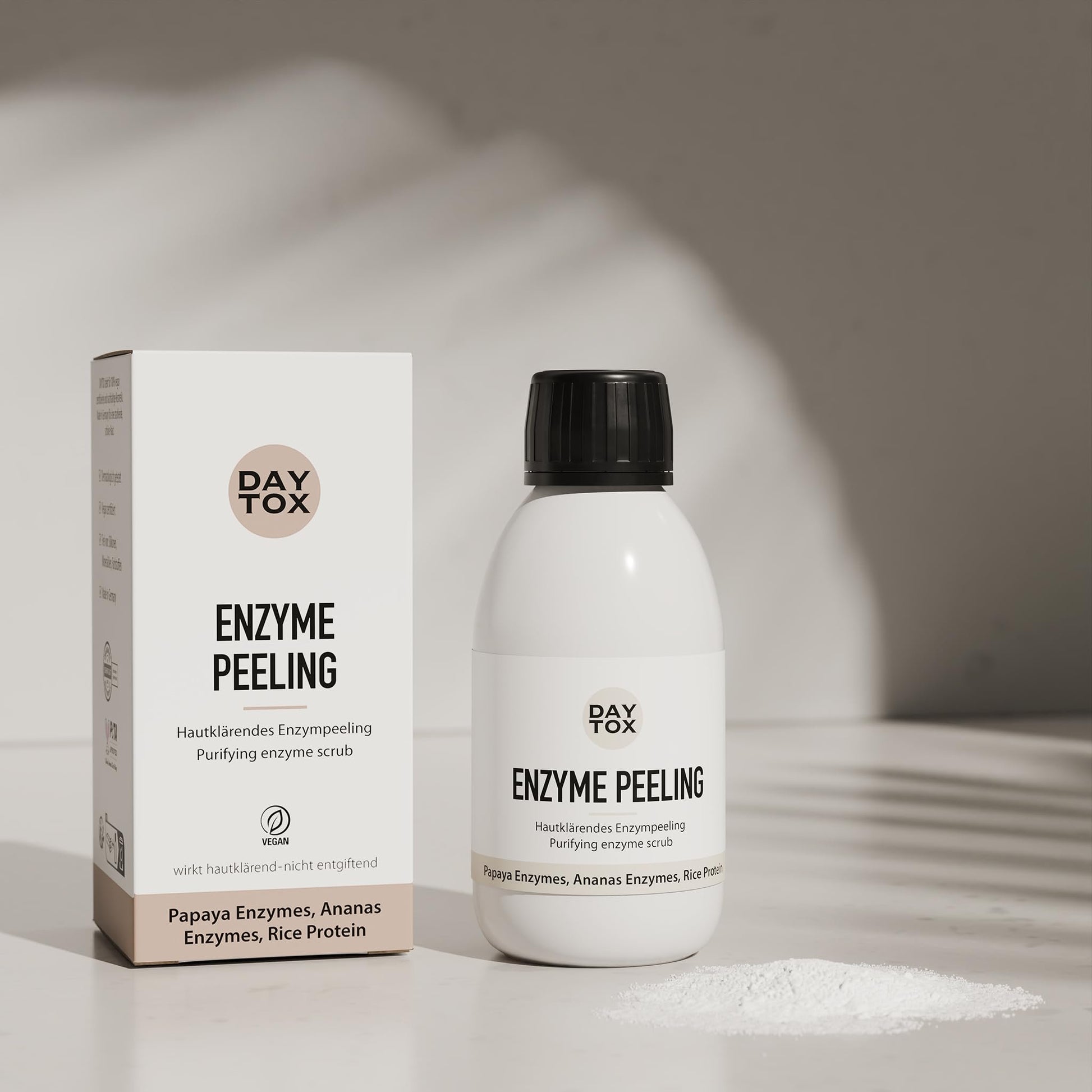 Weiße Flasche und weiße Produktverpackung des Daytox Enzyme Peeling auf hellem Untergrund mit Pulver.