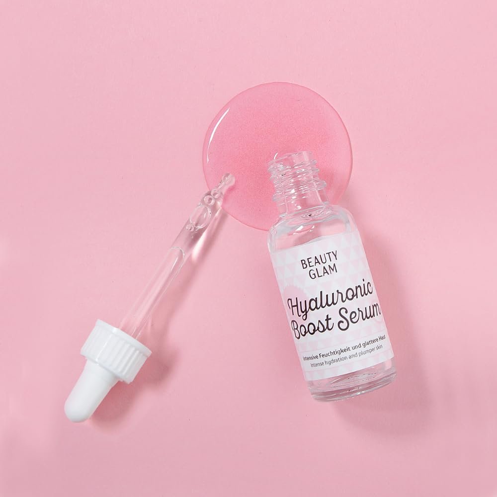 Offene Serumflasche mit Pipette und einem Tropfen pinker Flüssigkeit auf pinkem Hintergrund.