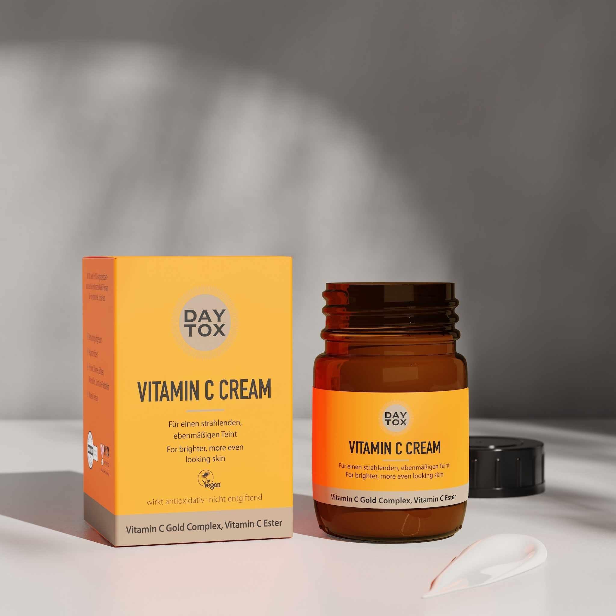 Orangefarbene Produktverpackung und offener Tiegel der DAYTOX Vitamin C Creme mit etwas Creme daneben.