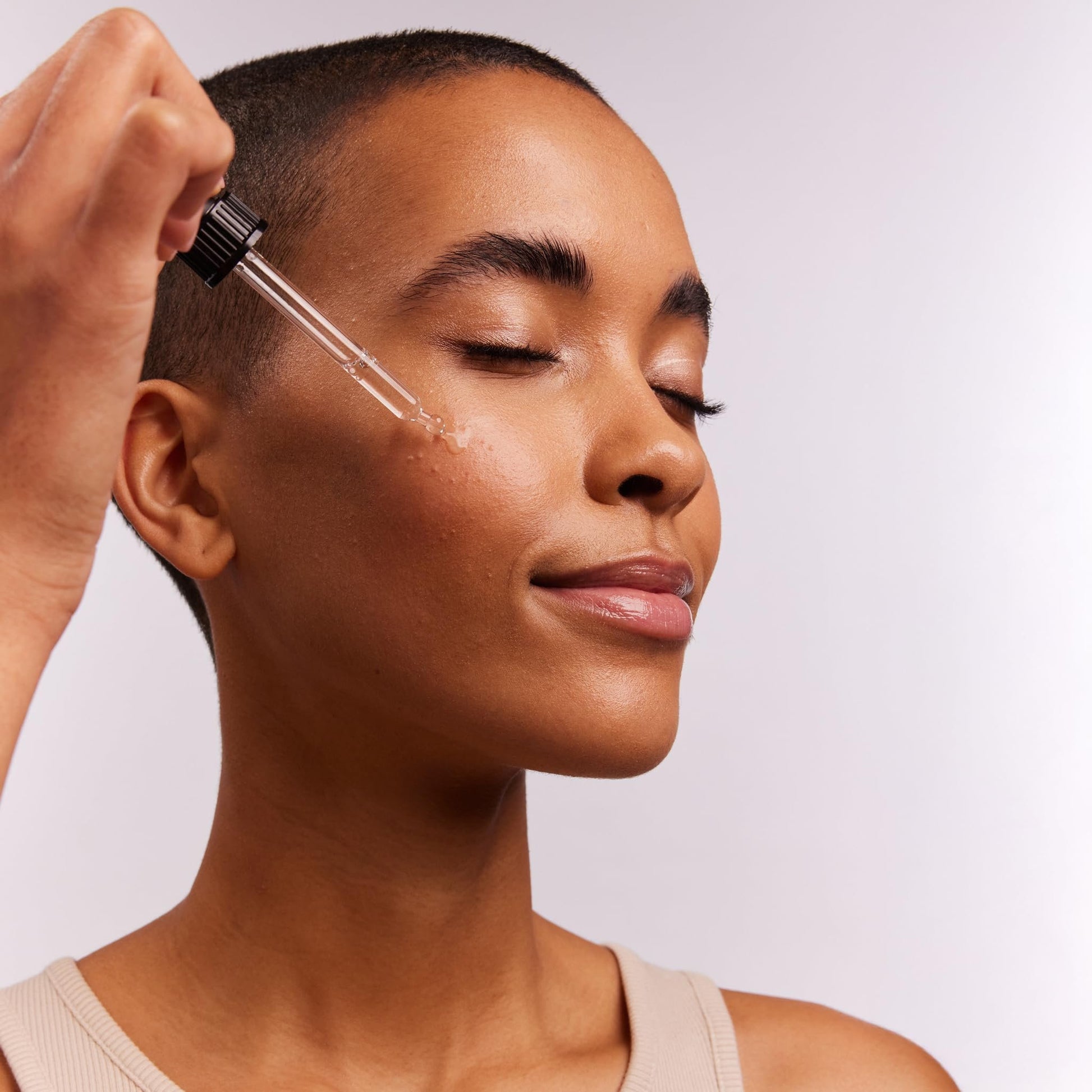 Eine Person mit kurzen Haaren trägt das Daytox Bakuchiol Oil Serum mit einer Pipette auf ihr Gesicht auf.