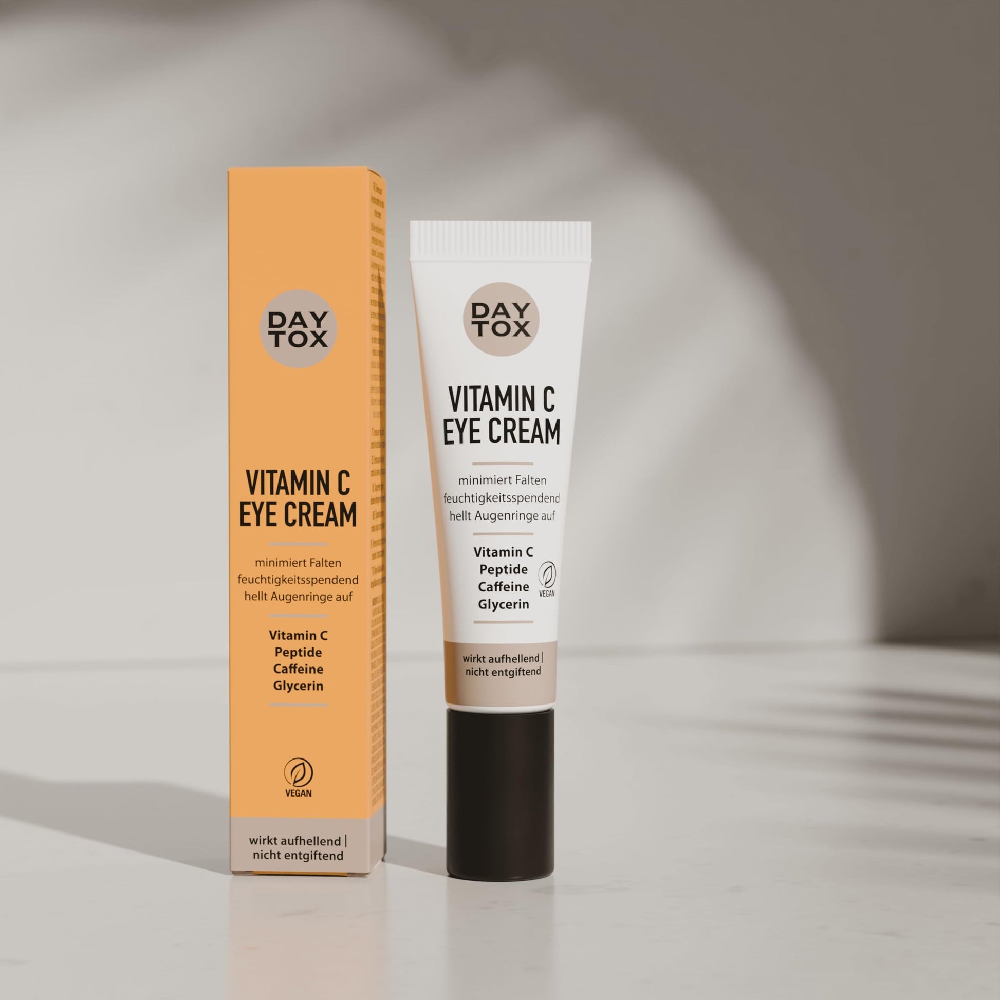 DAYTOX Vitamin C Augencreme Tube und orangefarbene Verpackung stehen aufrecht nebeneinander.